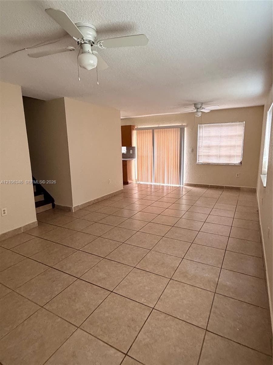 Open-concept interior featuring large-format ceramic tile flooring, dual ceiling fans, sliding glass doors, and recessed window treatments