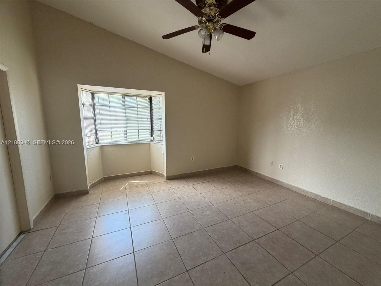Vaulted ceiling featuring a central multi-blade ceiling fan, expansive bay window, and large-format tile flooring