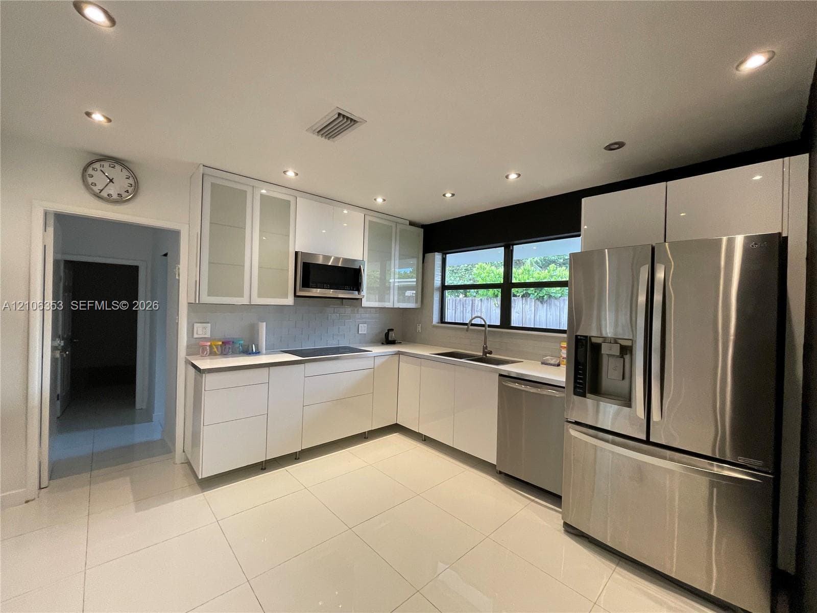 Modern kitchen featuring flat-panel white cabinetry, stainless steel appliances, recessed ceiling lighting, light-toned tile flooring, and a subway-style tile backsplash