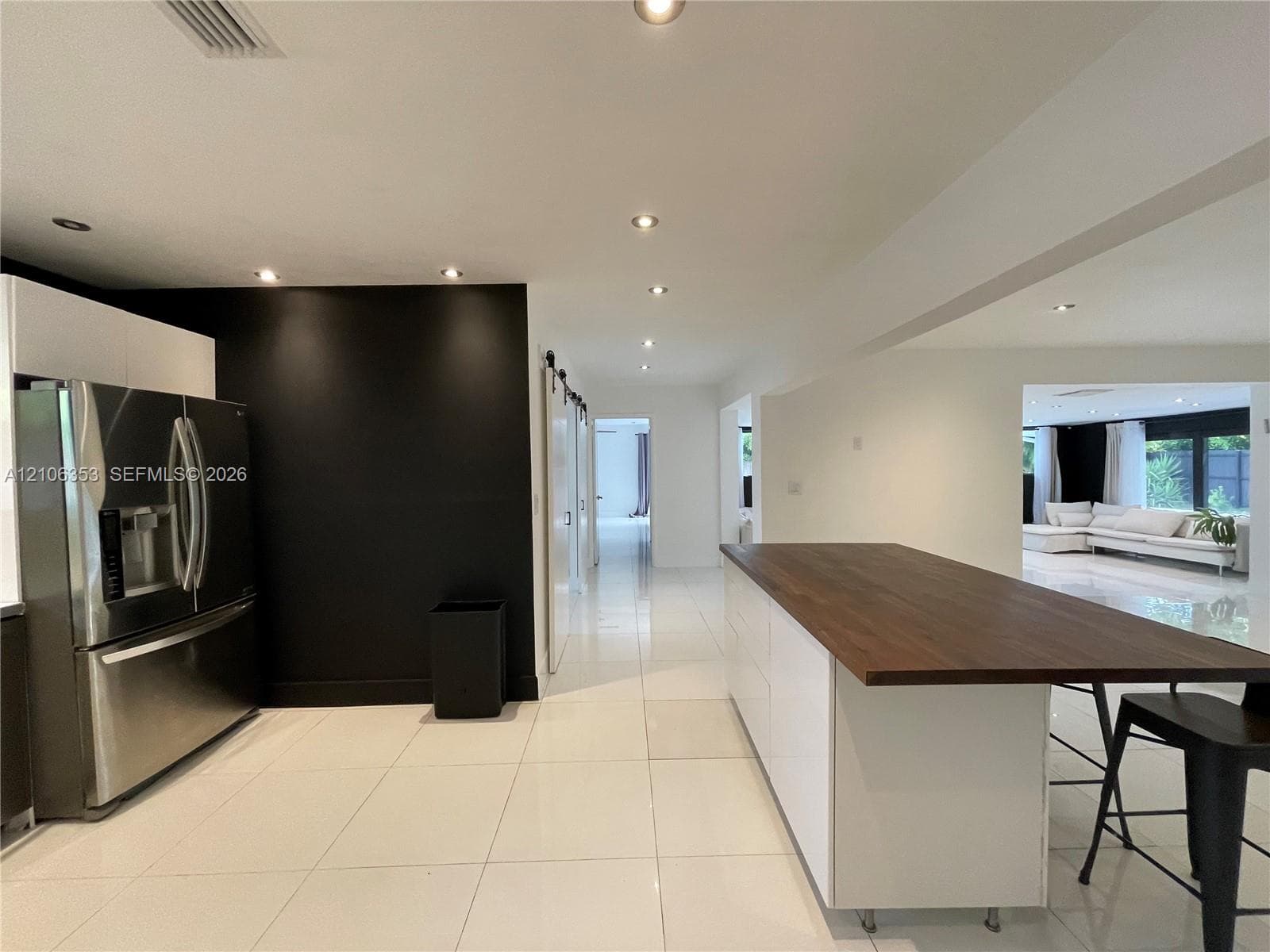 Kitchen featuring a white cabinetry island with a wood-finish countertop, high-gloss large-format tile flooring, stainless steel refrigerator, and recessed lighting