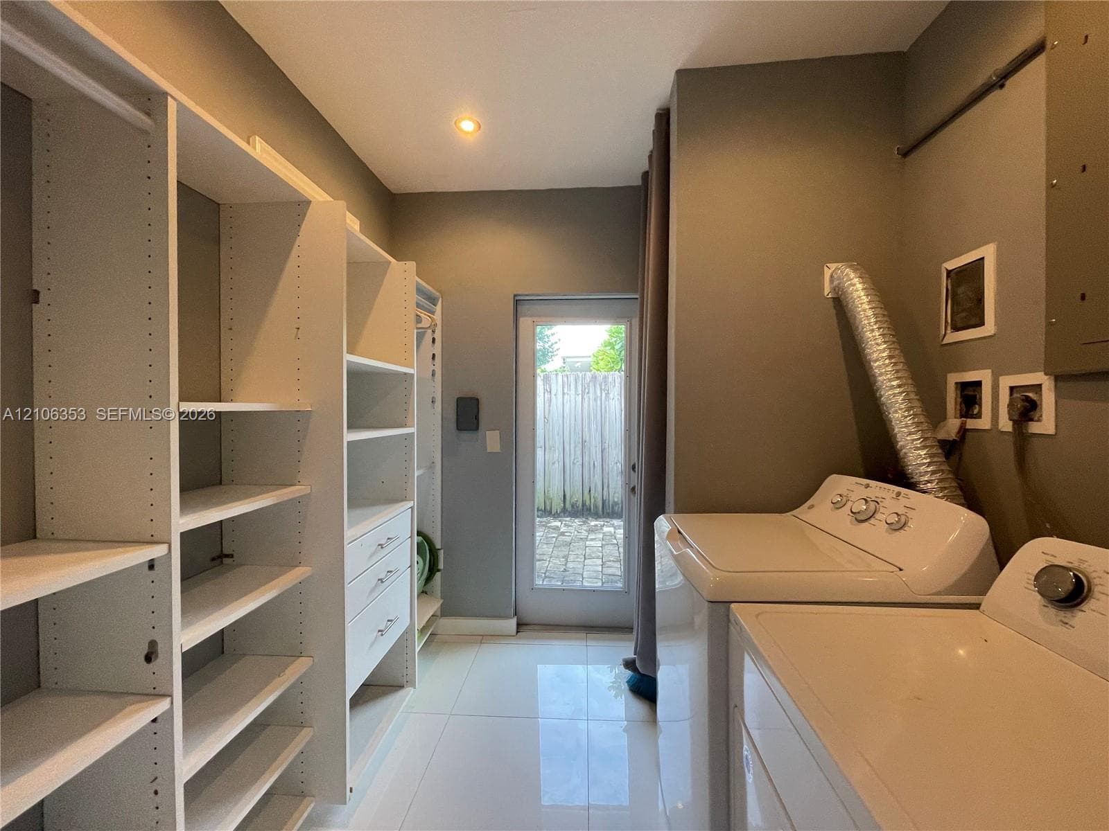 Custom built-in white shelving system with integrated storage drawers, polished tile flooring, and glass-paneled exterior door