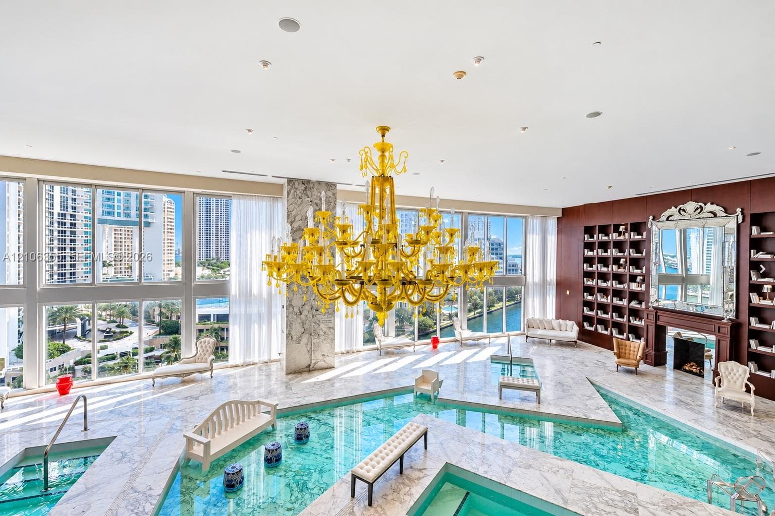 Indoor pool area featuring natural stone flooring, floor-to-ceiling windows, an expansive yellow chandelier, built-in shelving, and a decorative fireplace