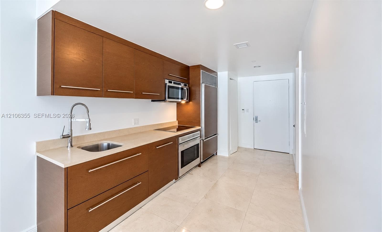 Kitchen featuring wood-finish cabinetry, solid surface countertops, stainless steel integrated refrigerator, built-in electric cooktop, and tile flooring