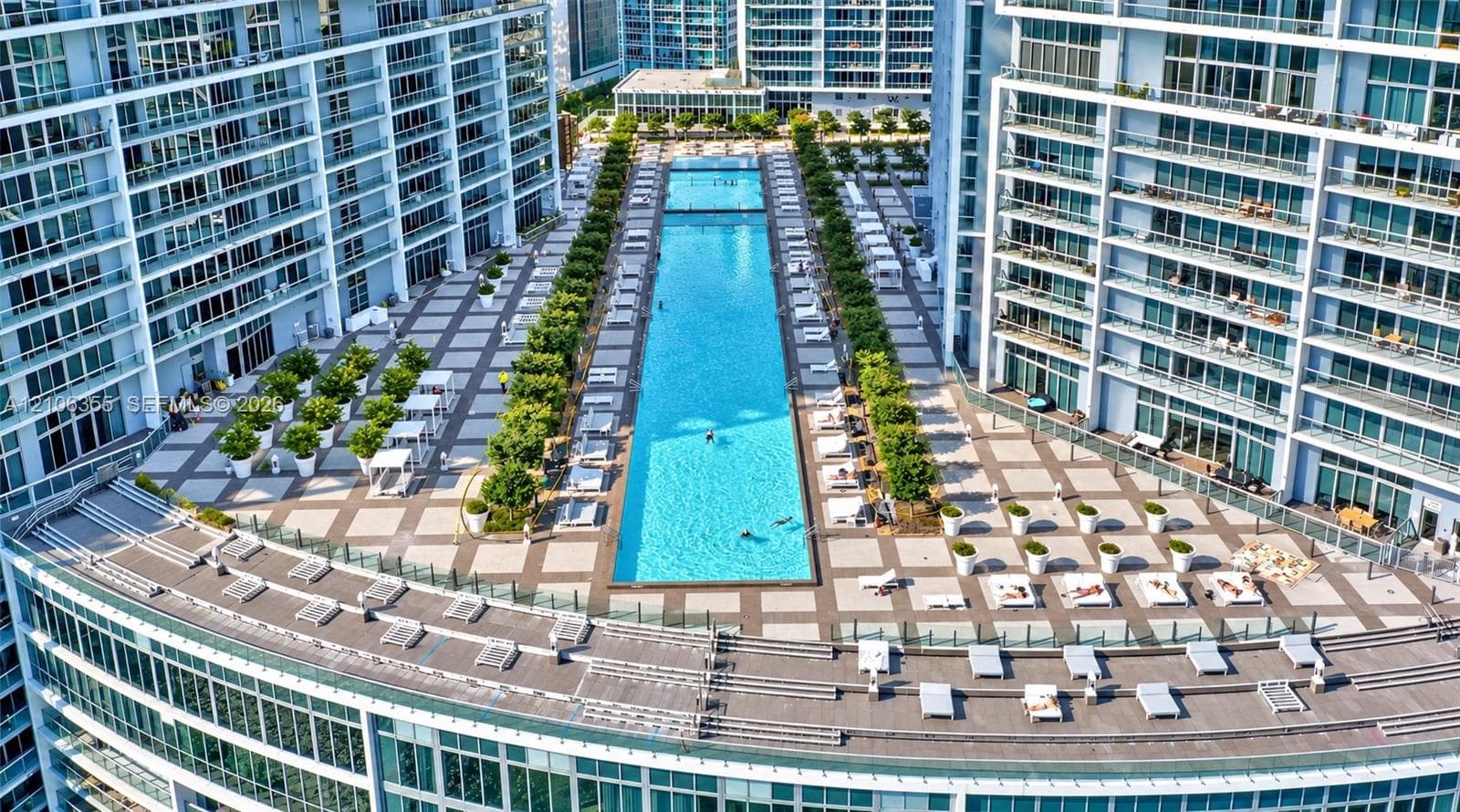 Expansive elevated terrace featuring a linear swimming pool, tiled hardscaping, manicured landscaping, and glass balcony railings