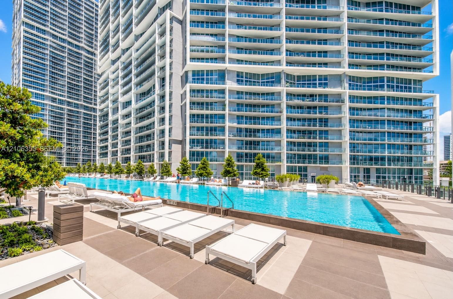 Infinity-edge swimming pool featuring a tiled deck, concrete surround, and structured landscaping