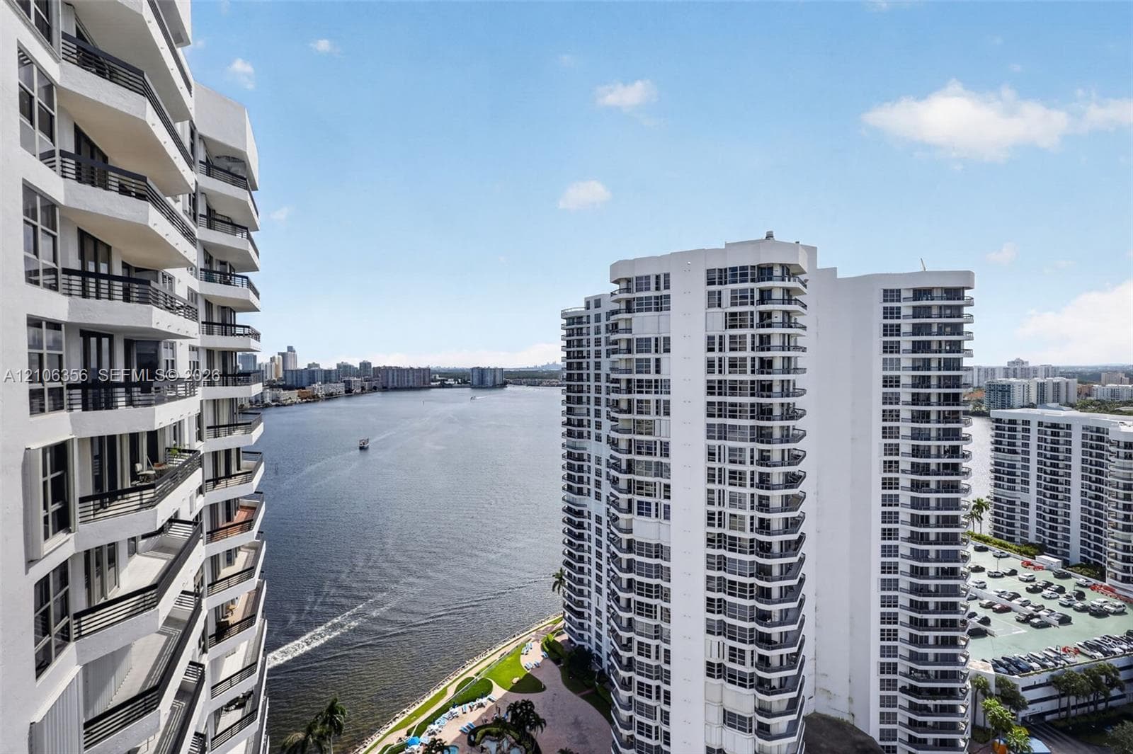 High-rise building featuring stacked balconies with dark metal railings, glass-paneled entryways, and expansive waterfront scenery