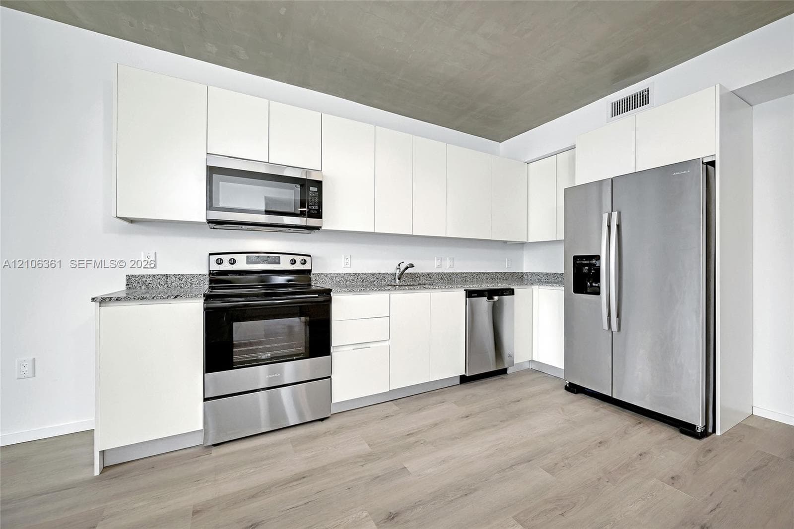 Kitchen featuring sleek white cabinetry, stone-finish countertops, stainless steel appliances, and wood-finish flooring under a concrete ceiling