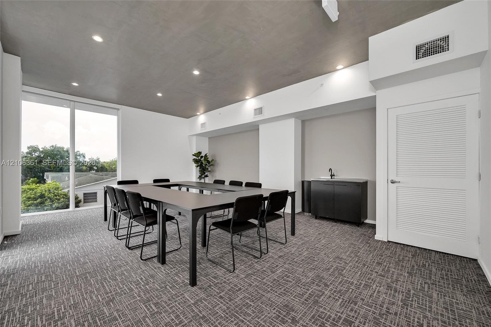 Floor-to-ceiling windows, recessed lighting, patterned carpeting, and a wet bar featuring dark cabinetry with a matte black faucet