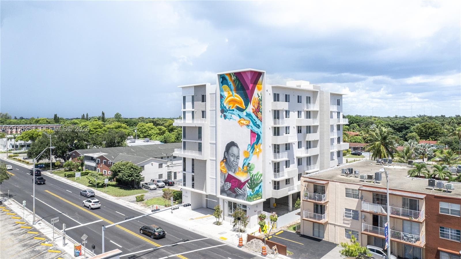 Multi-story residential building featuring a large-scale exterior mural, private balconies, and ground-level covered parking