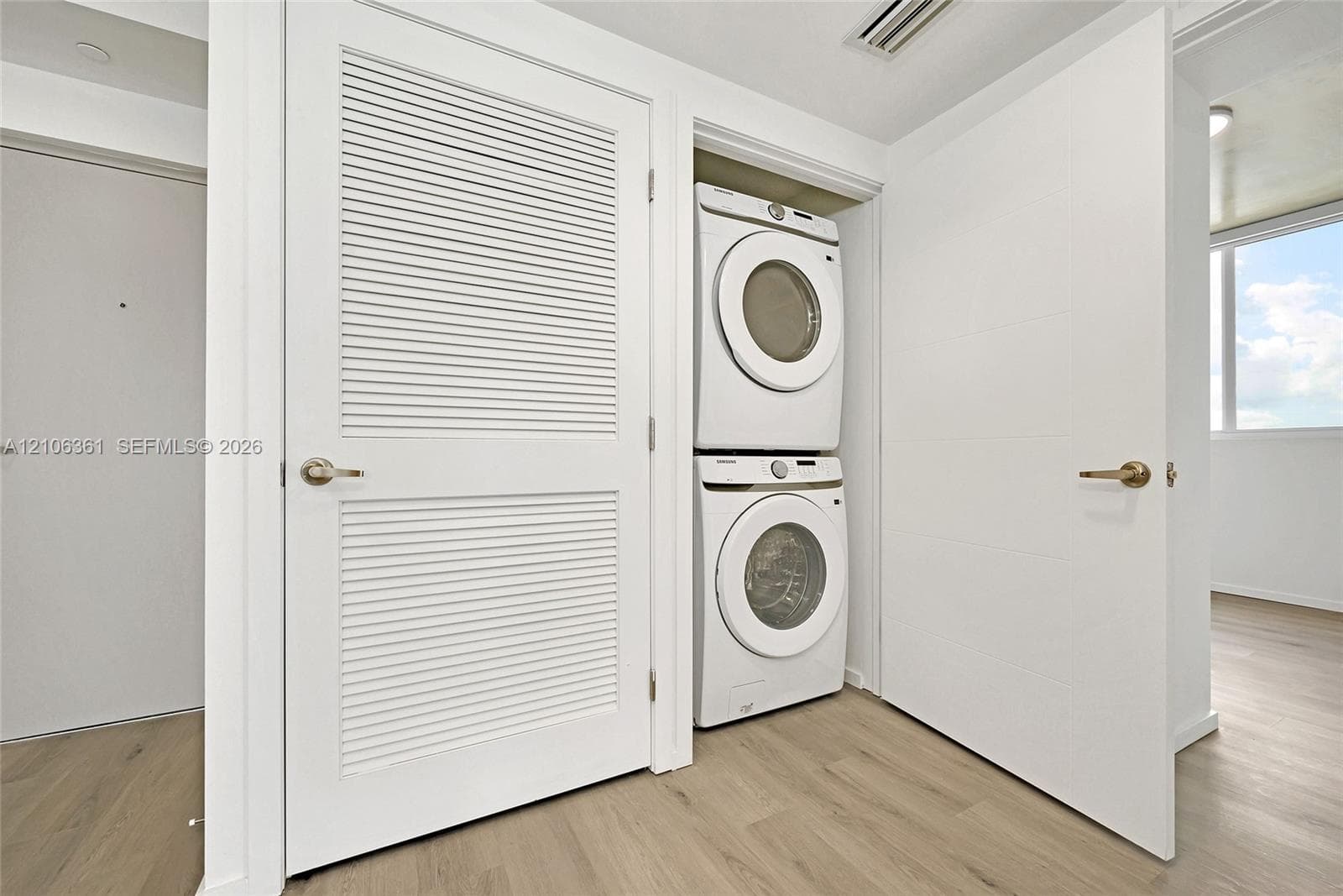 Laundry closet featuring a stacked washer and dryer unit, louvered swing door, solid-core interior doors with metallic hardware, and wood-finish flooring