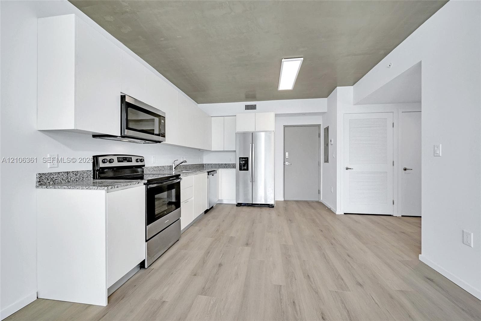 Kitchen featuring white flat-panel cabinetry, stone-finish countertops, stainless steel appliances, and wood-finish flooring under a concrete-texture ceiling