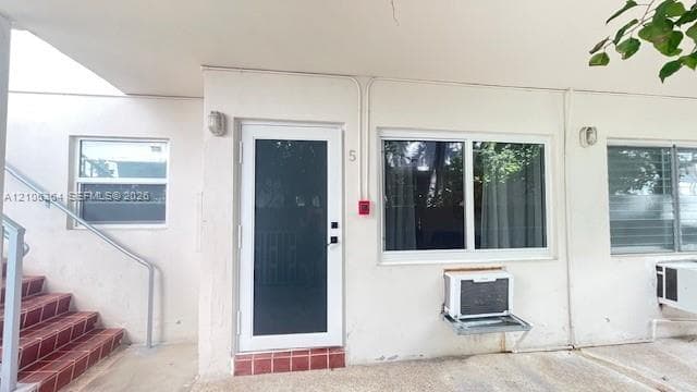 Exterior entryway featuring a white-framed glass storm door, white stucco facade, tiled stair treads, and sliding glass windows