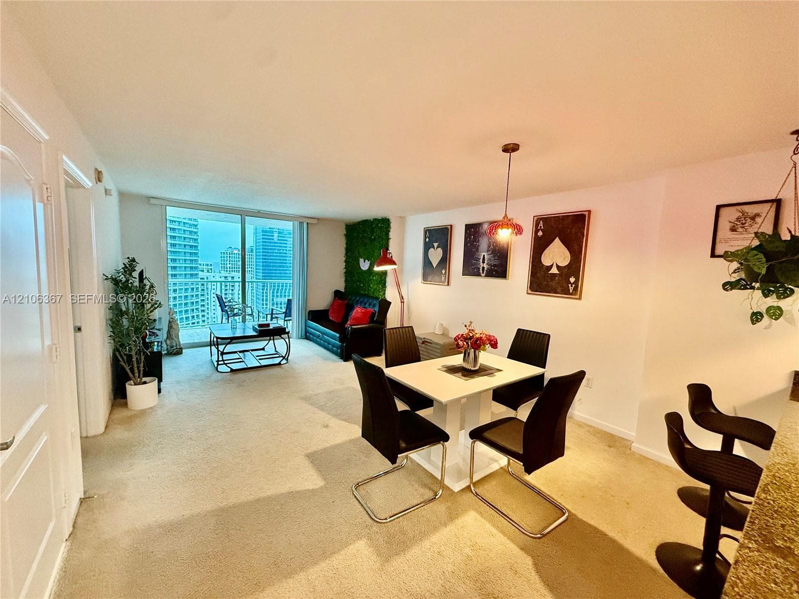Open-concept main living area featuring floor-to-ceiling glass sliding doors, neutral carpeting, and a built-in kitchen breakfast bar