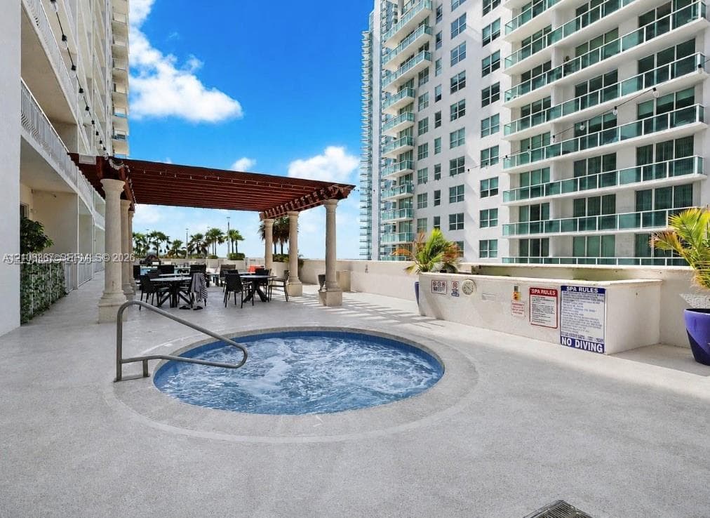 Outdoor terrace featuring a recessed circular hot tub, concrete flooring, and a shaded pergola supported by stone columns
