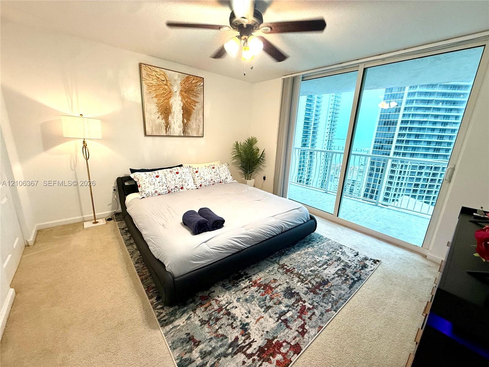 Floor-to-ceiling sliding glass doors, private balcony access, neutral wall finishes, carpeted flooring, and a multi-blade ceiling fan with integrated lighting