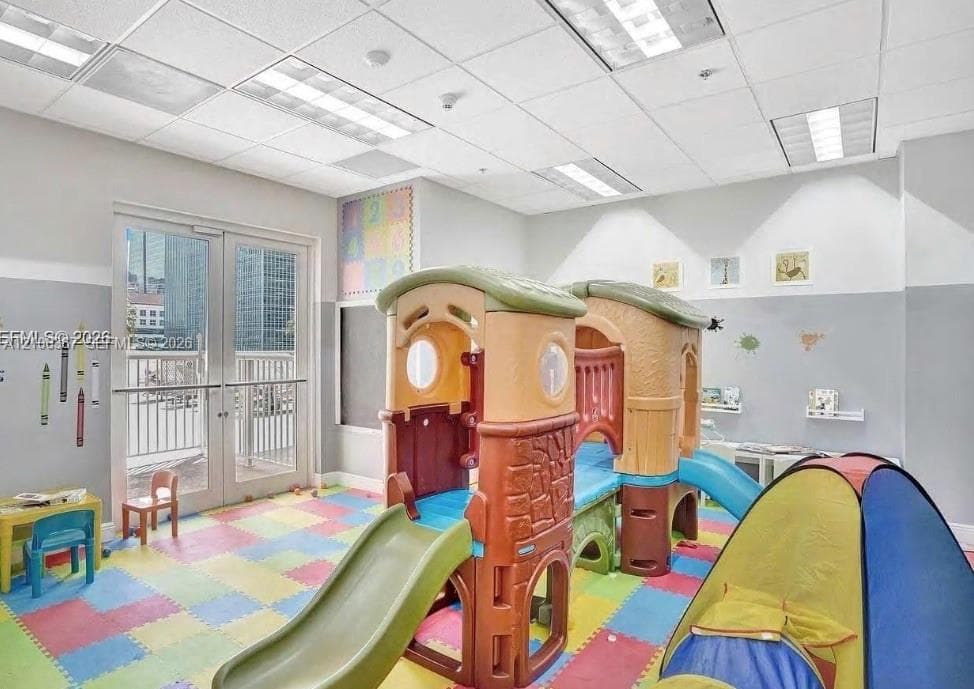 Multi-purpose room featuring drop ceiling with recessed lighting, integrated wall-mounted chalkboard, and glass-paneled double doors providing outdoor access
