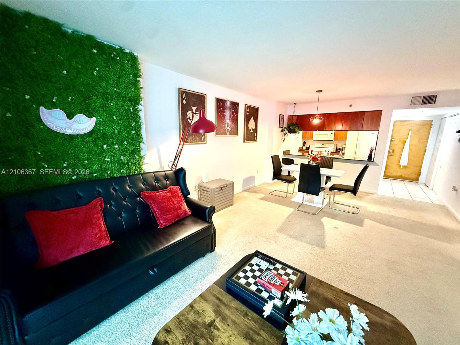 Open-concept interior featuring a decorative wall accent, kitchen with wood-finish cabinetry, and neutral carpeting