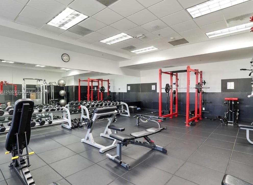 Fitness facility featuring rubberized flooring, mirrored walls, recessed grid ceiling lighting, and black wall paneling