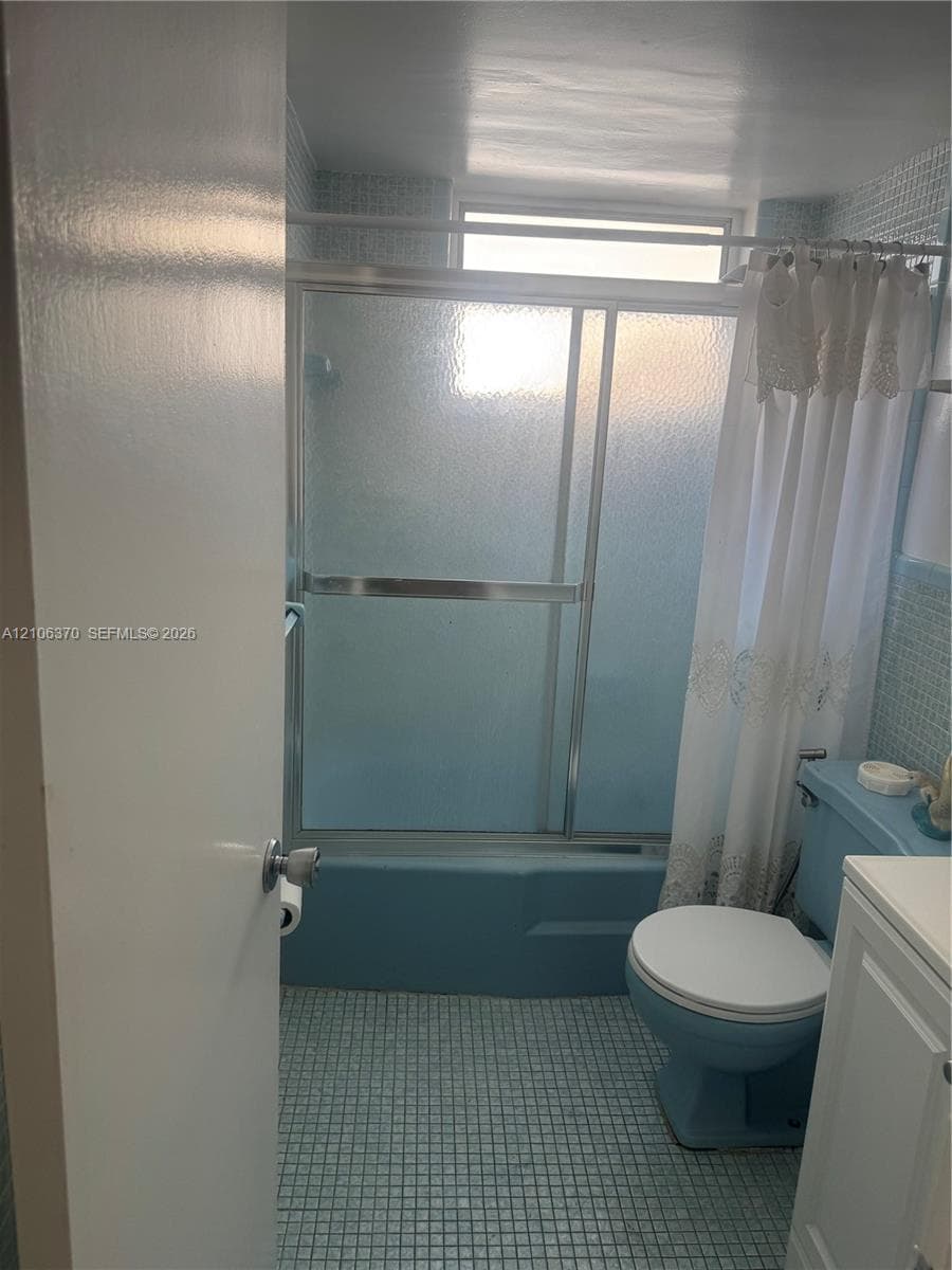 Bathroom featuring a combination bathtub and shower with a sliding glass enclosure, mosaic-tiled walls, grid-patterned floor tiling, and a vanity cabinet