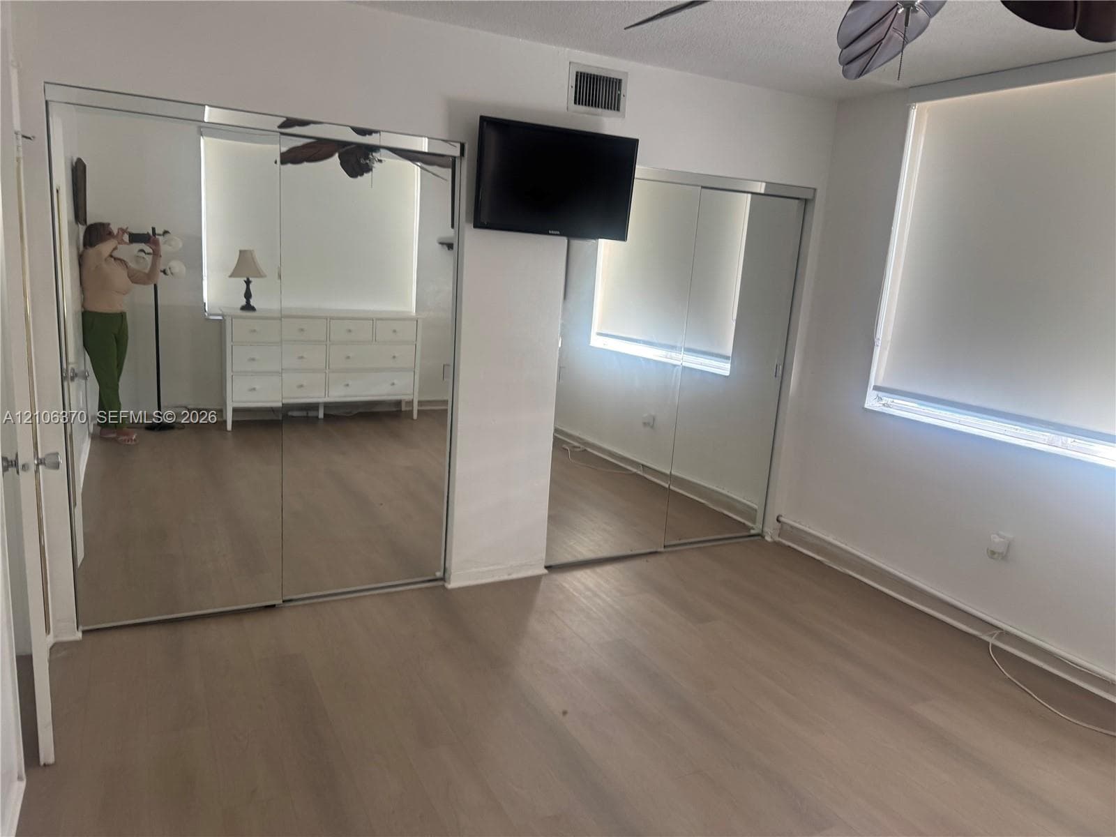 Room featuring wood-finish flooring, dual mirrored sliding closet doors, and windows with roller shades