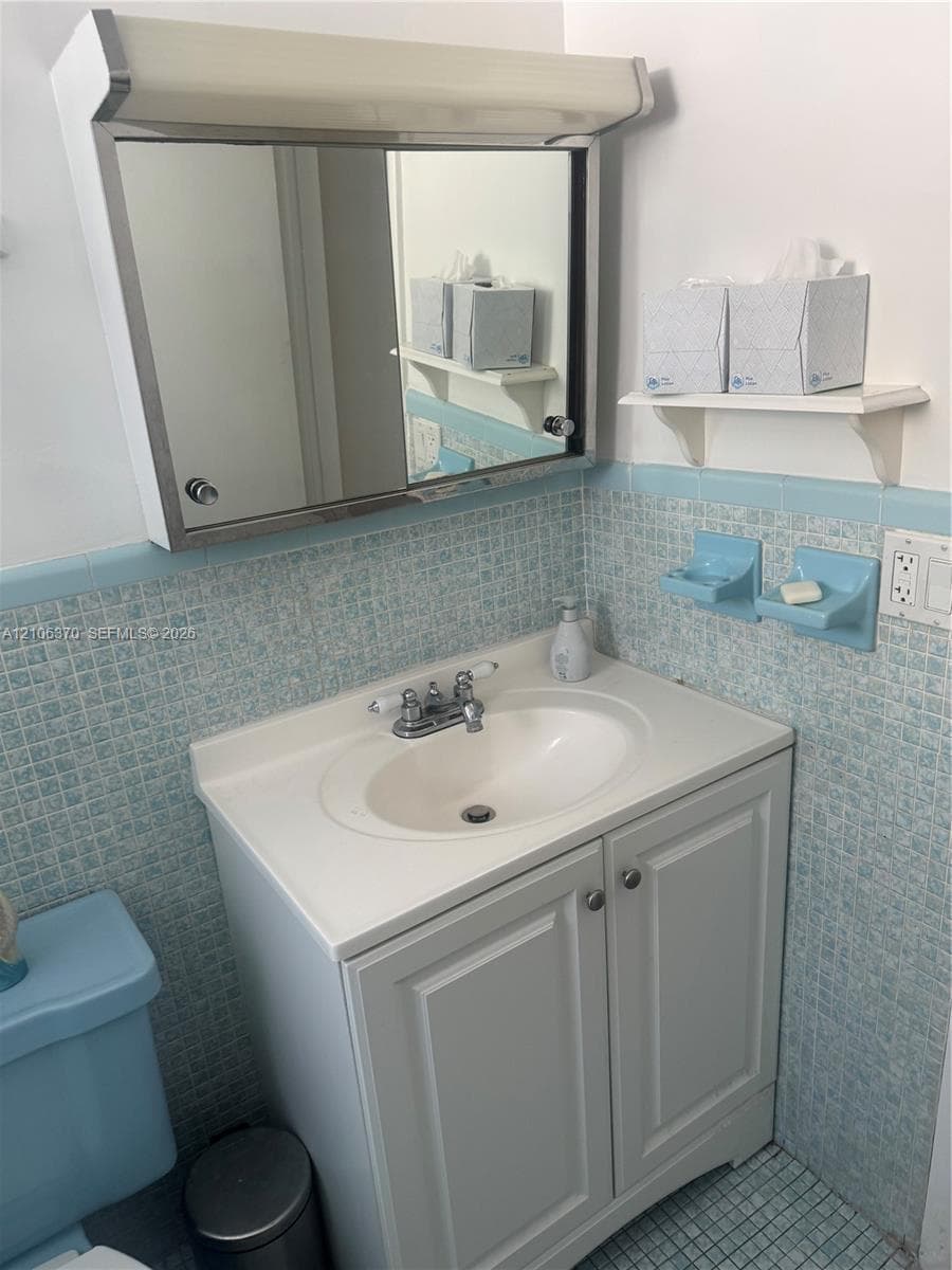 Vanity cabinet with a white basin and chrome-finish dual-handle faucet, metal-frame medicine cabinet, and wall-mounted shelving featuring blue mosaic tile detailing