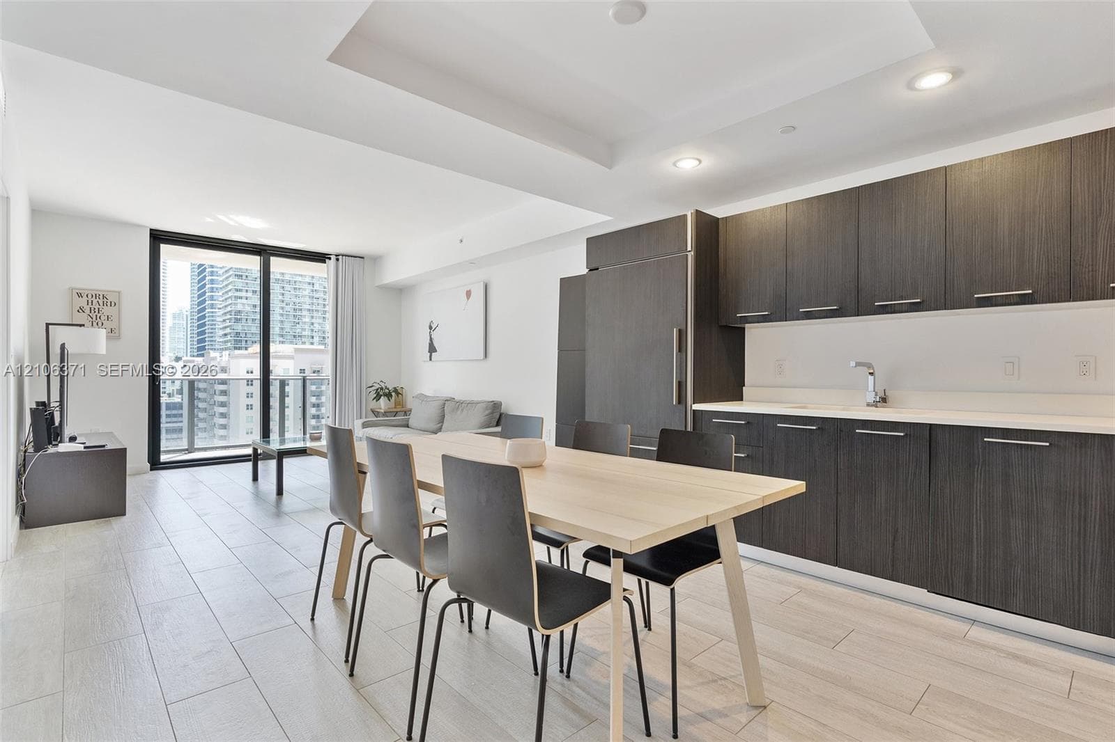 Modern kitchen featuring dark-toned cabinetry, light-toned countertops, recessed lighting, wood-finish flooring, and a glass sliding door leading to an outdoor balcony