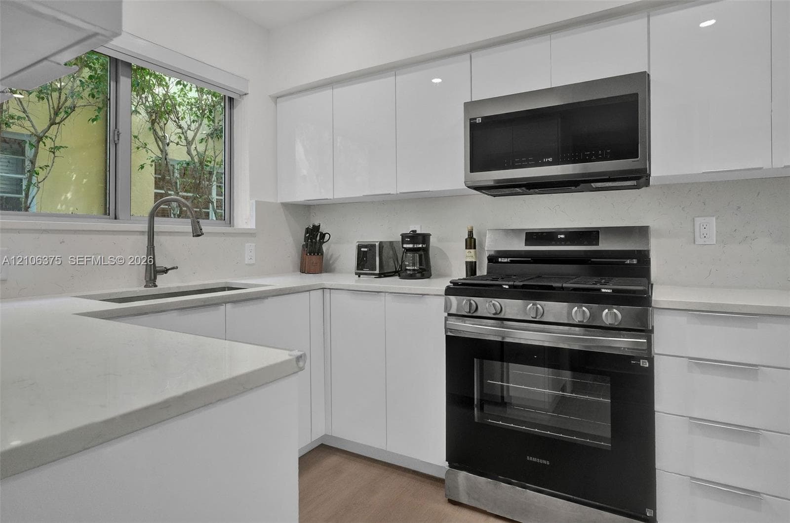 Kitchen featuring high-gloss white cabinetry, solid surface countertops, a stainless steel gas range, a built-in microwave, and an undermount sink with a gooseneck faucet