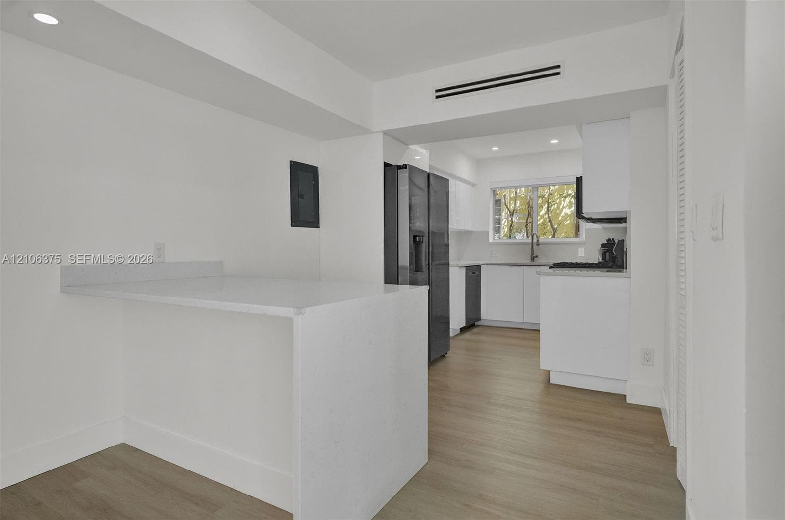 Kitchen featuring crisp white cabinetry, light-toned wood-finish flooring, recessed lighting, and a solid-surface peninsula countertop