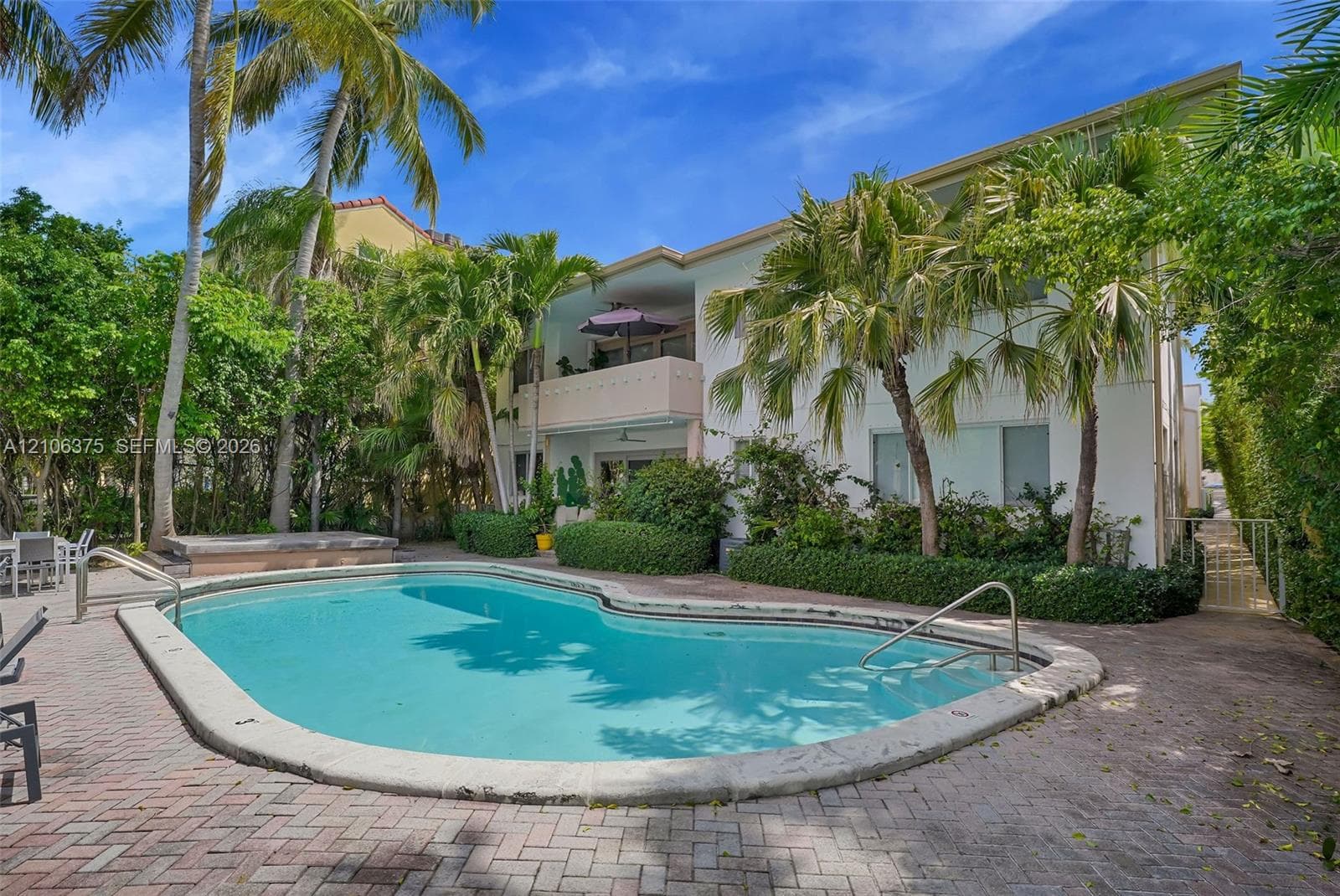 In-ground swimming pool with a concrete surround, paver patio, elevated balcony, and mature landscaping