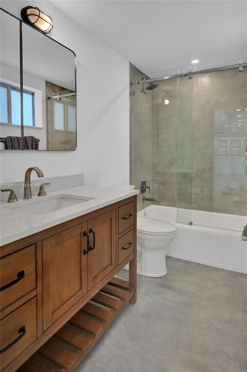 Bathroom featuring a wooden vanity with open shelving, a white stone countertop, an integrated rectangular sink, a sliding glass tub enclosure, and matte finish plumbing fixtures