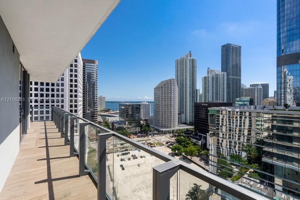 Private balcony with wood-finish tile flooring and transparent glass railing overlooking a metropolitan skyline and waterfront