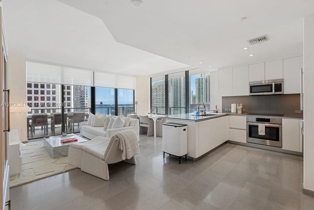 Open-concept kitchen featuring flat-panel cabinetry, stainless steel appliances, and stone countertops, complemented by floor-to-ceiling windows and tile flooring