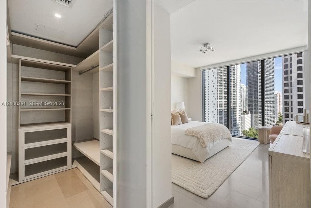Custom-built walk-in closet featuring floor-to-ceiling shelving, integrated drawer units, and hanging rods, accompanied by a room with floor-to-ceiling windows and large-format tile flooring