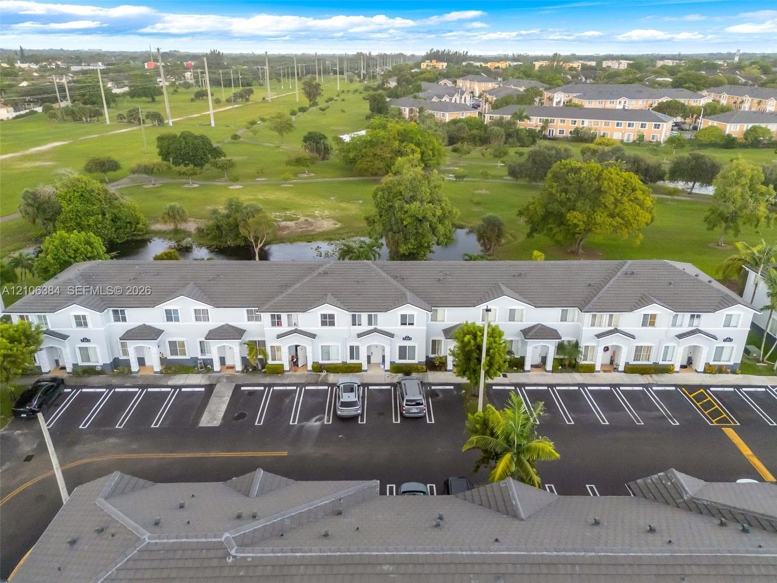 Multi-unit building exterior featuring a hip roof, stucco facade, covered entryways, and surface parking