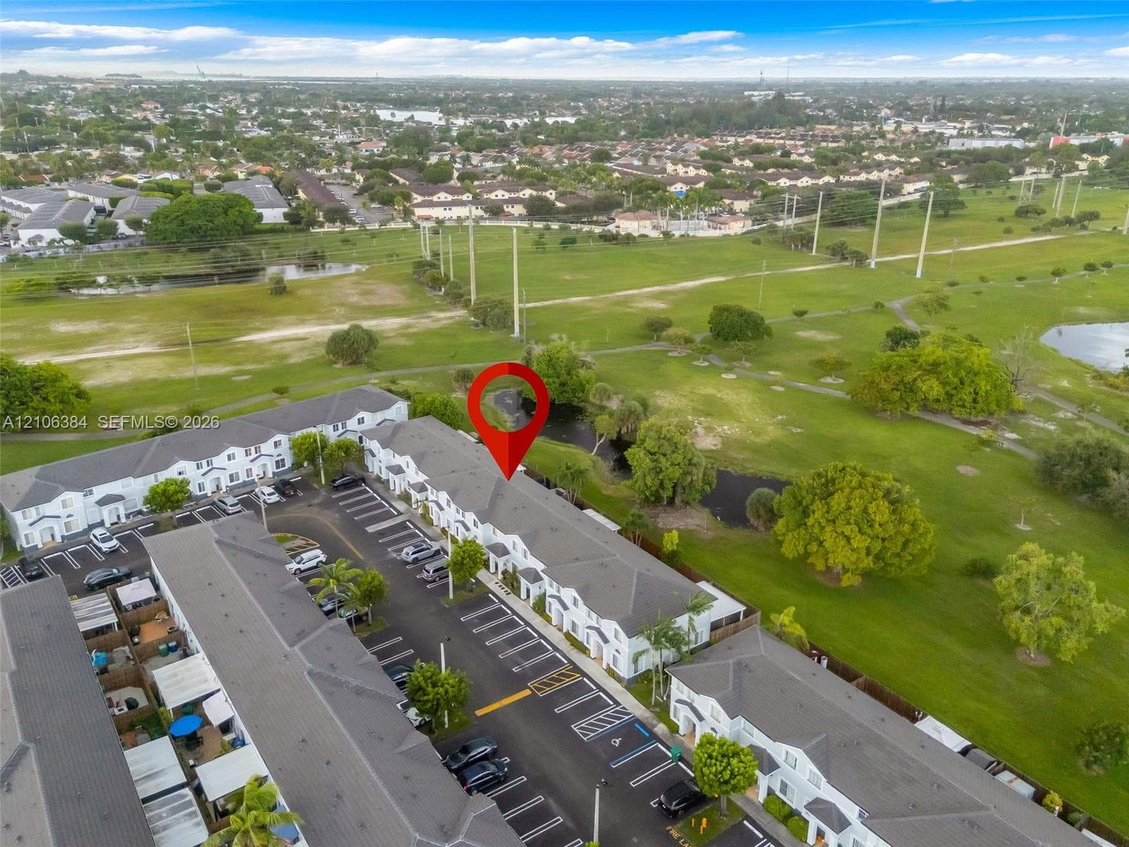 Aerial perspective featuring multi-story townhouse structures with shingle roofing, paved surface parking, and manicured green space backdrop
