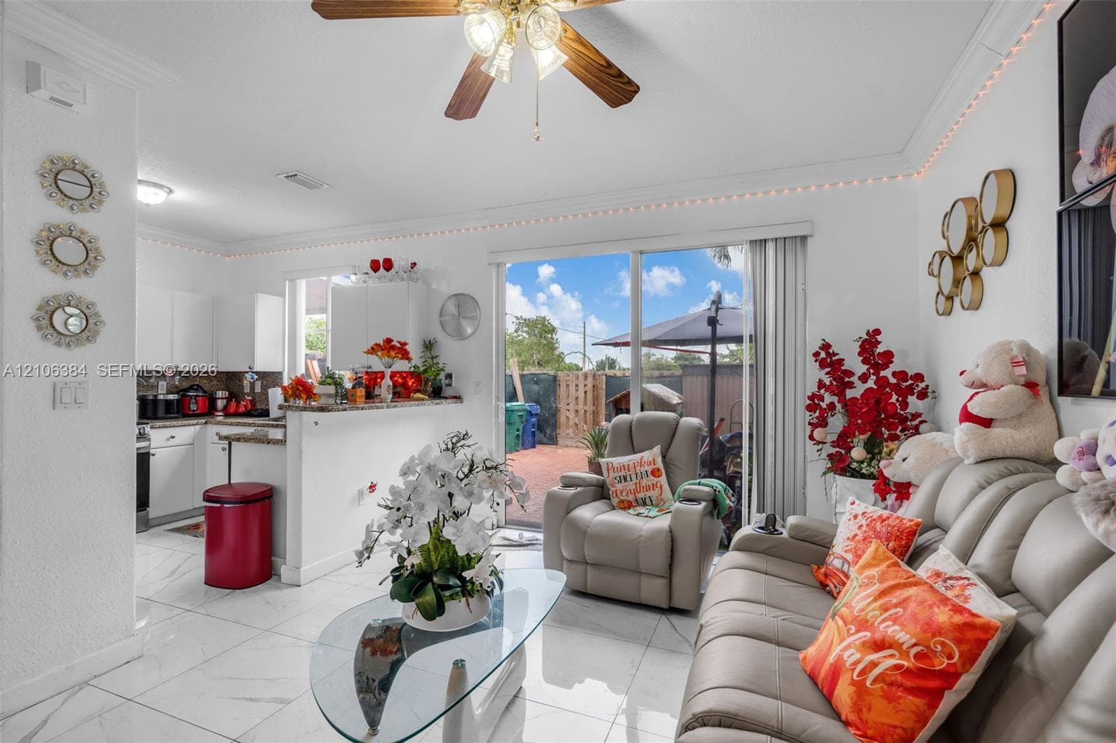 Open-concept interior featuring large-format tile flooring, a kitchen breakfast bar, sliding glass doors to the exterior, and a ceiling fan