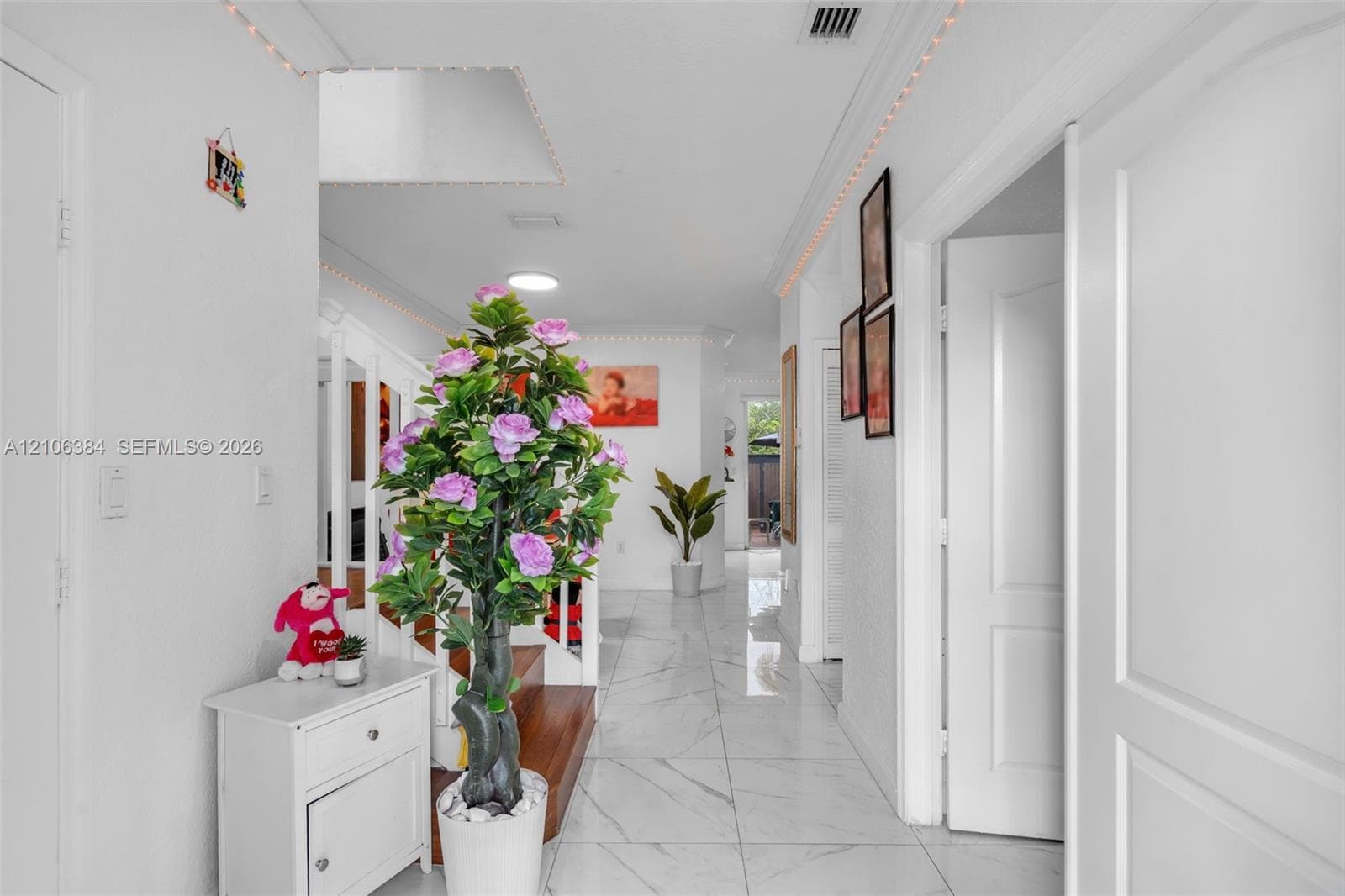 Interior hallway featuring white tile flooring with veining detail, recessed lighting, crown molding, and a staircase with wood treads and white balusters