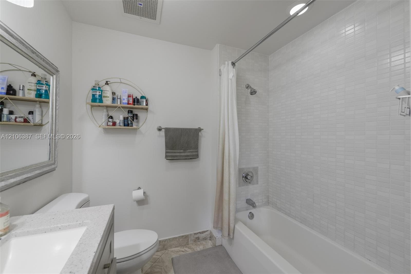 Bathroom featuring a vanity with a light-toned countertop, a shower-tub combination with white tile surround, and a metal towel bar