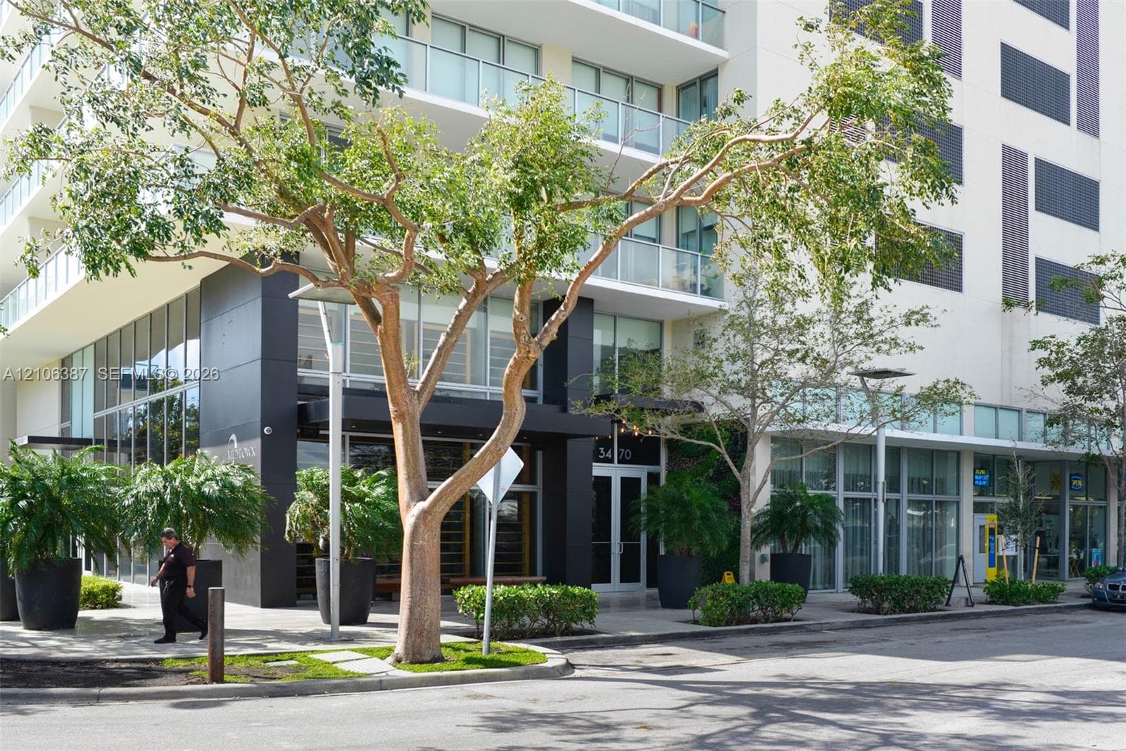 Multi-story exterior facade featuring floor-to-ceiling glass windows, glass-panel balcony railings, black paneling accents, and exterior hardscaping