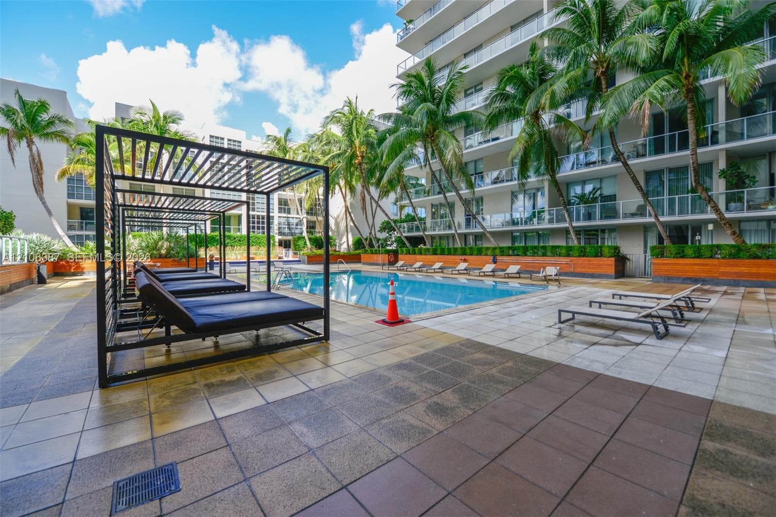 Swimming pool featuring a multi-tiered tile deck, built-in metal pergolas, perimeter planter boxes with mature palm trees, and glass-railed balconies