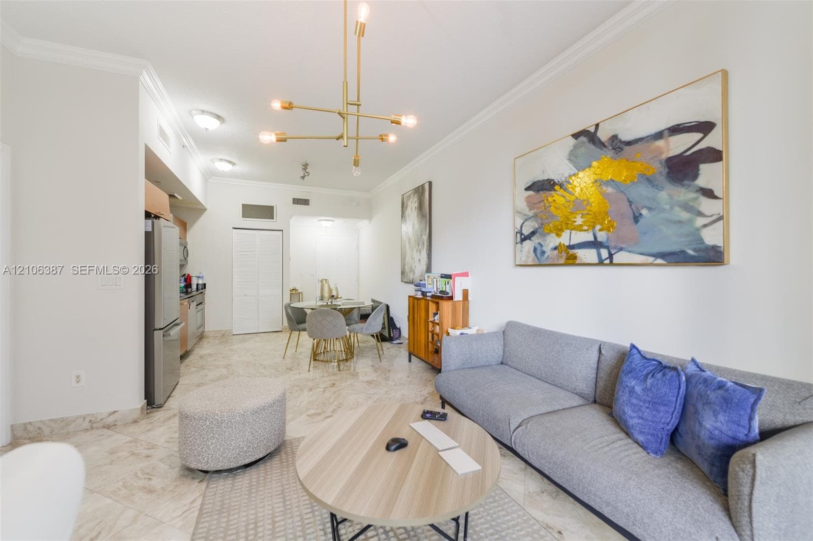 Open-concept space featuring polished stone flooring, crown molding, modern multi-arm brass chandelier, and built-in stainless steel appliances