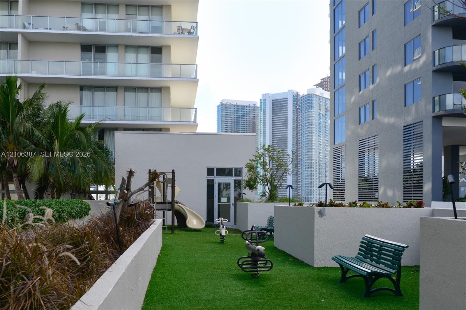 Outdoor recreation area featuring artificial turf, fixed playground equipment, built-in benches, and concrete retaining walls