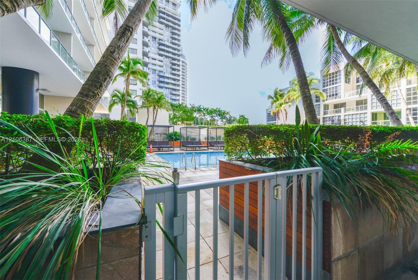 Outdoor swimming pool featuring a metal security gate, stone tile deck, raised wood-panel landscaping planters, and mature palm trees