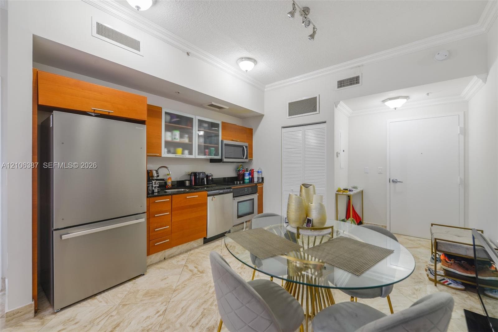 Kitchen featuring wood-veneer cabinetry, stainless steel appliances, glass-front upper cabinets, dark solid-surface countertops, and diagonal-patterned stone flooring