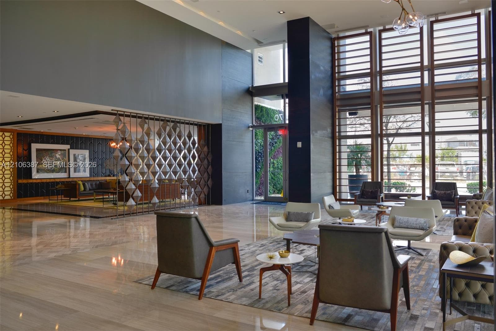Grand lobby featuring floor-to-ceiling windows, polished stone flooring, decorative metal room divider, and accent wall with vertical wood paneling
