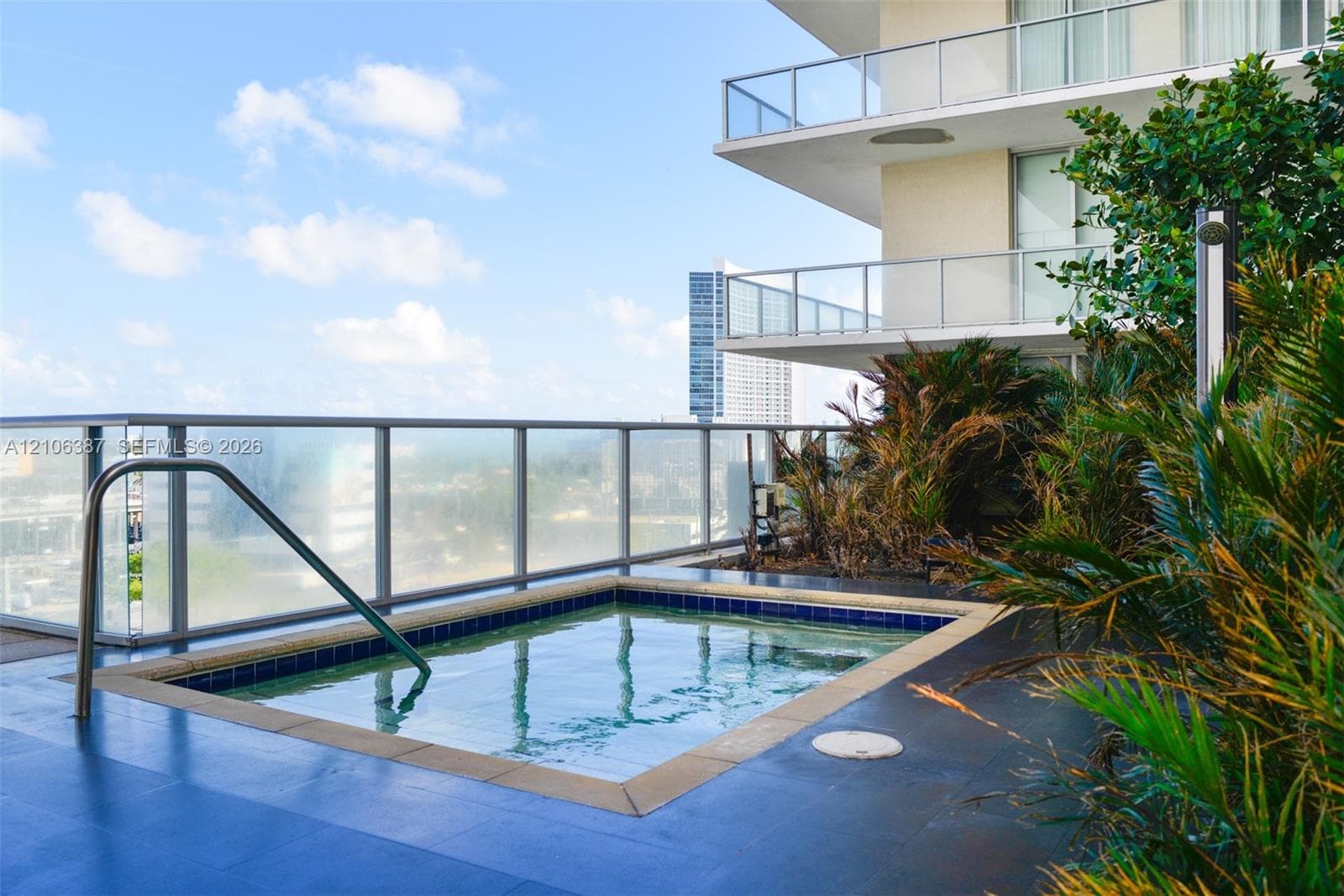 Outdoor terrace featuring an in-ground spa, tile surround, glass railing, and integrated landscaping