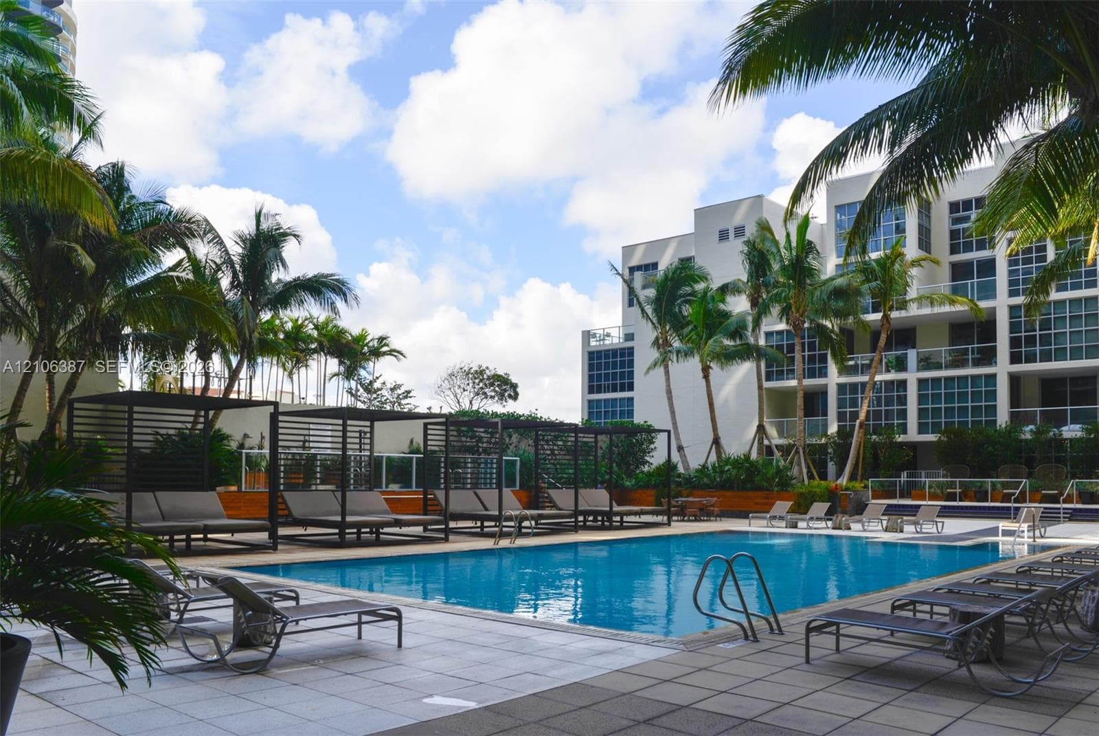 Swimming pool with surrounding tiled deck, structured metal cabanas, and mature palm trees
