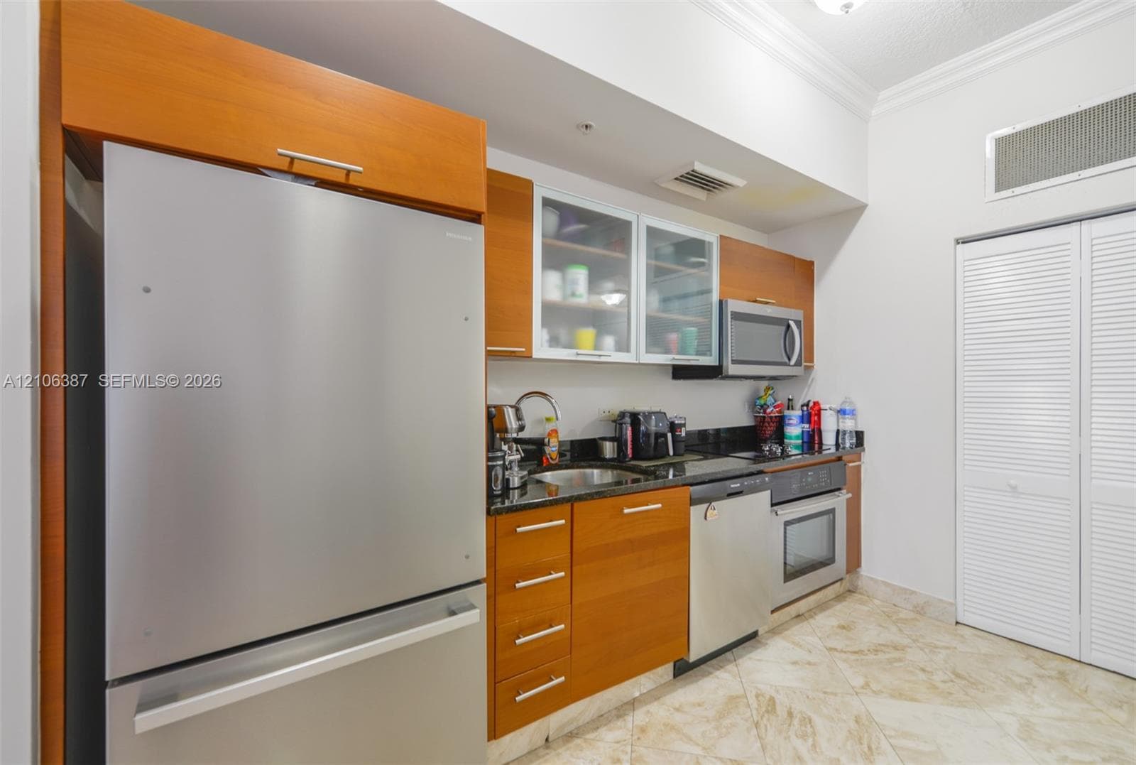 Kitchen featuring wood cabinetry, stone countertops, stainless steel appliances, glass-front upper cabinets, and tile flooring