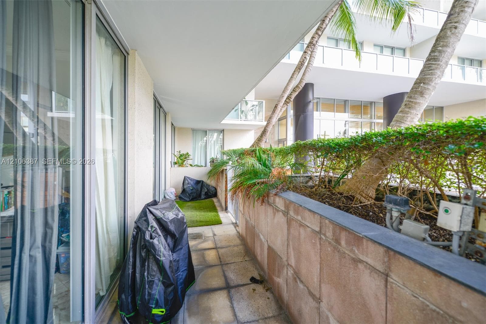 Covered balcony featuring large-format stone floor tiles, expansive glass sliding doors, a masonry perimeter wall with a stone cap, and built-in landscape planters