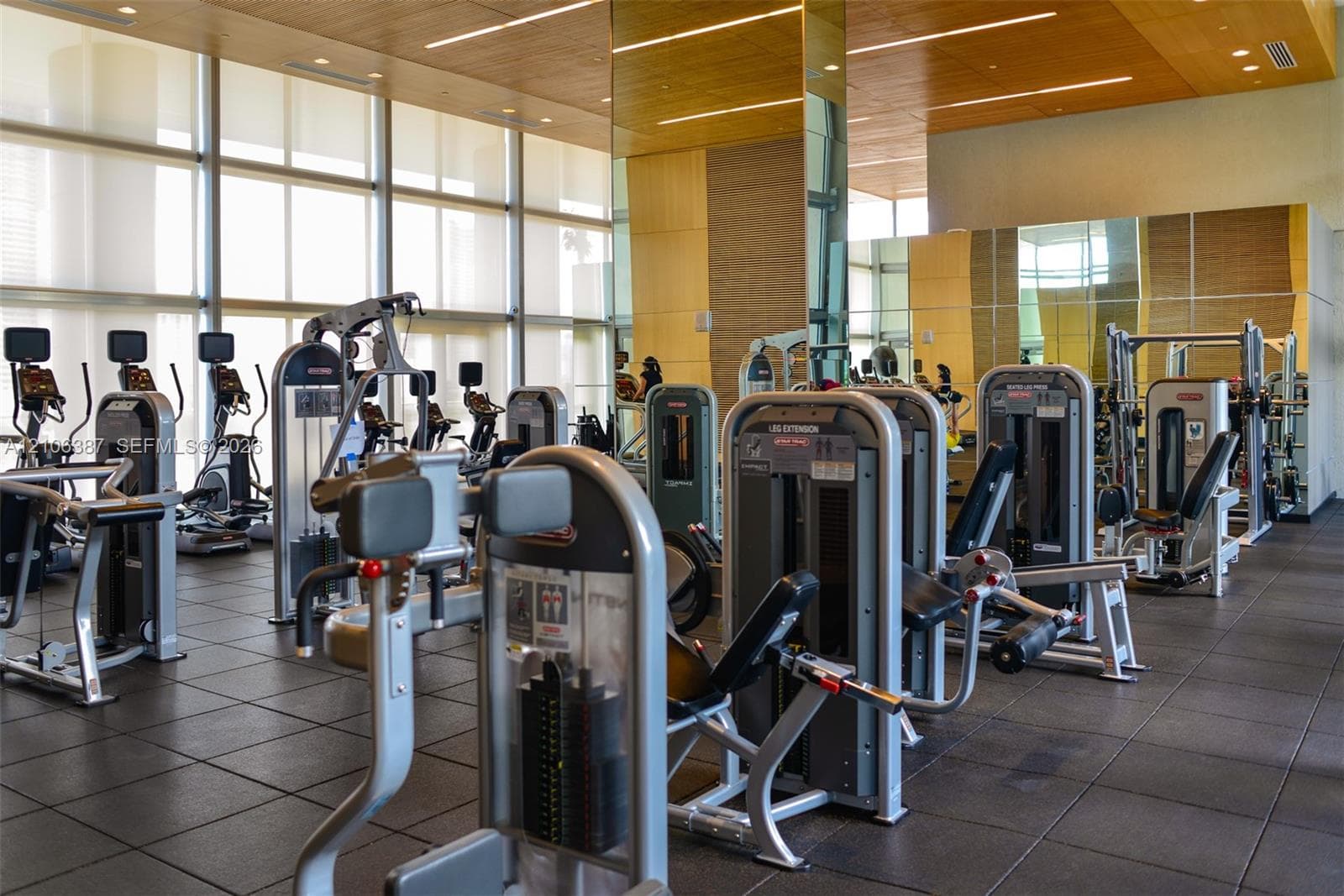 Fitness center featuring floor-to-ceiling windows, wood-paneled ceilings, mirrored accent walls, and rubberized tile flooring